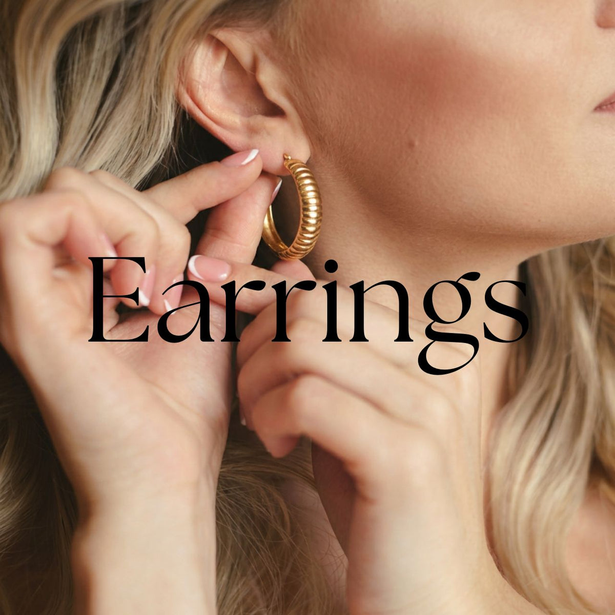 Silver charm hoop earrings displayed on a white branch against a soft blush background, featuring eye, smiley face, star, sunburst, and round charm designs.