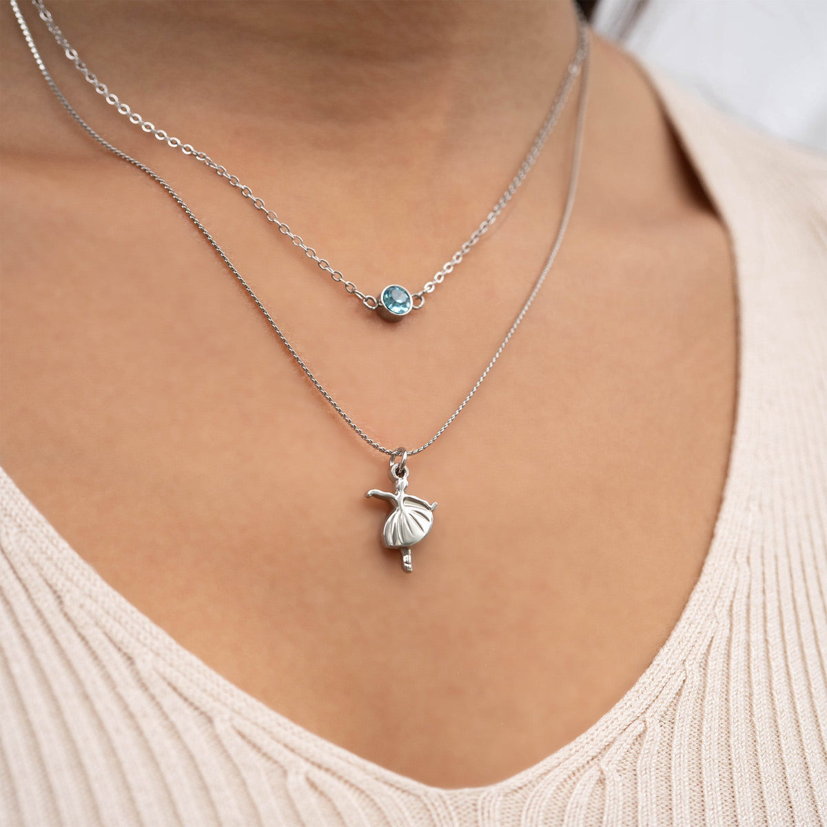 Close-up of a woman wearing two silver necklaces with shell and blue gemstone pendants.