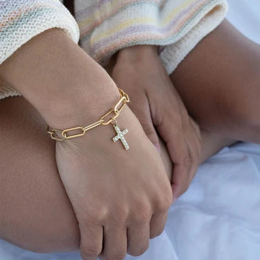 Gold bracelet with a cross charm on a person's wrist.