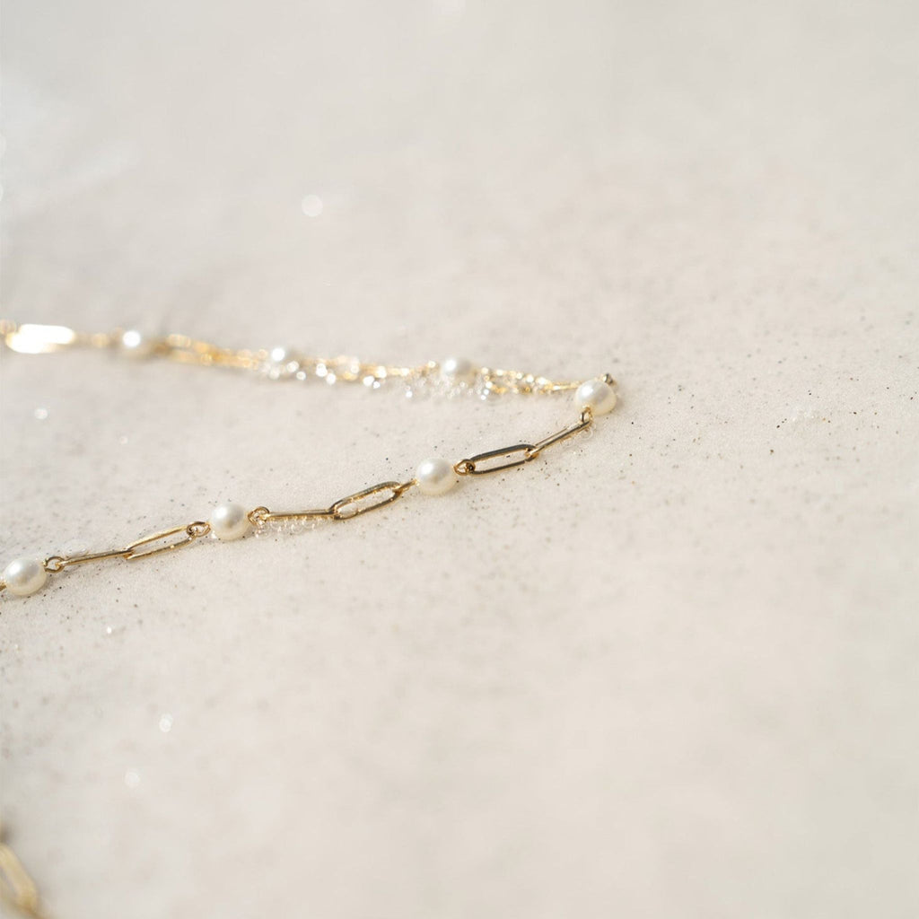 Gold chain necklace with pearls on a light beige background