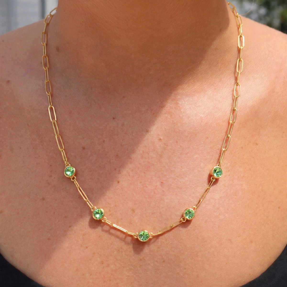 A gold chain necklace with five small round green gemstones spaced along the front, shown worn on a person's neck and upper chest.