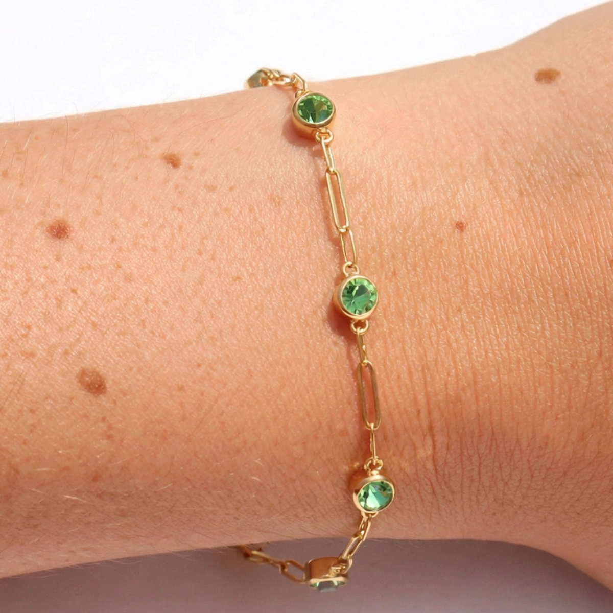 A delicate gold chain bracelet with three round green gemstones, shown worn on a person's wrist.