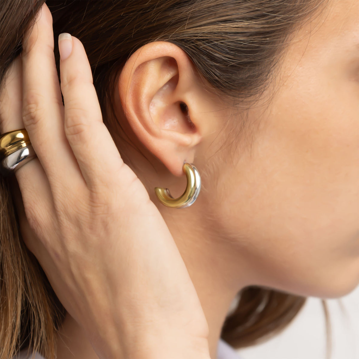Mixed metal side-by-side huggie earrings worn on the ear