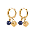 A pair of gold huggie hoop earrings with dangling charms. Each earring features a gold hoop, a small gold disc charm with an evil eye design, a small clear crystal, and a dark blue sodalite sphere bead.