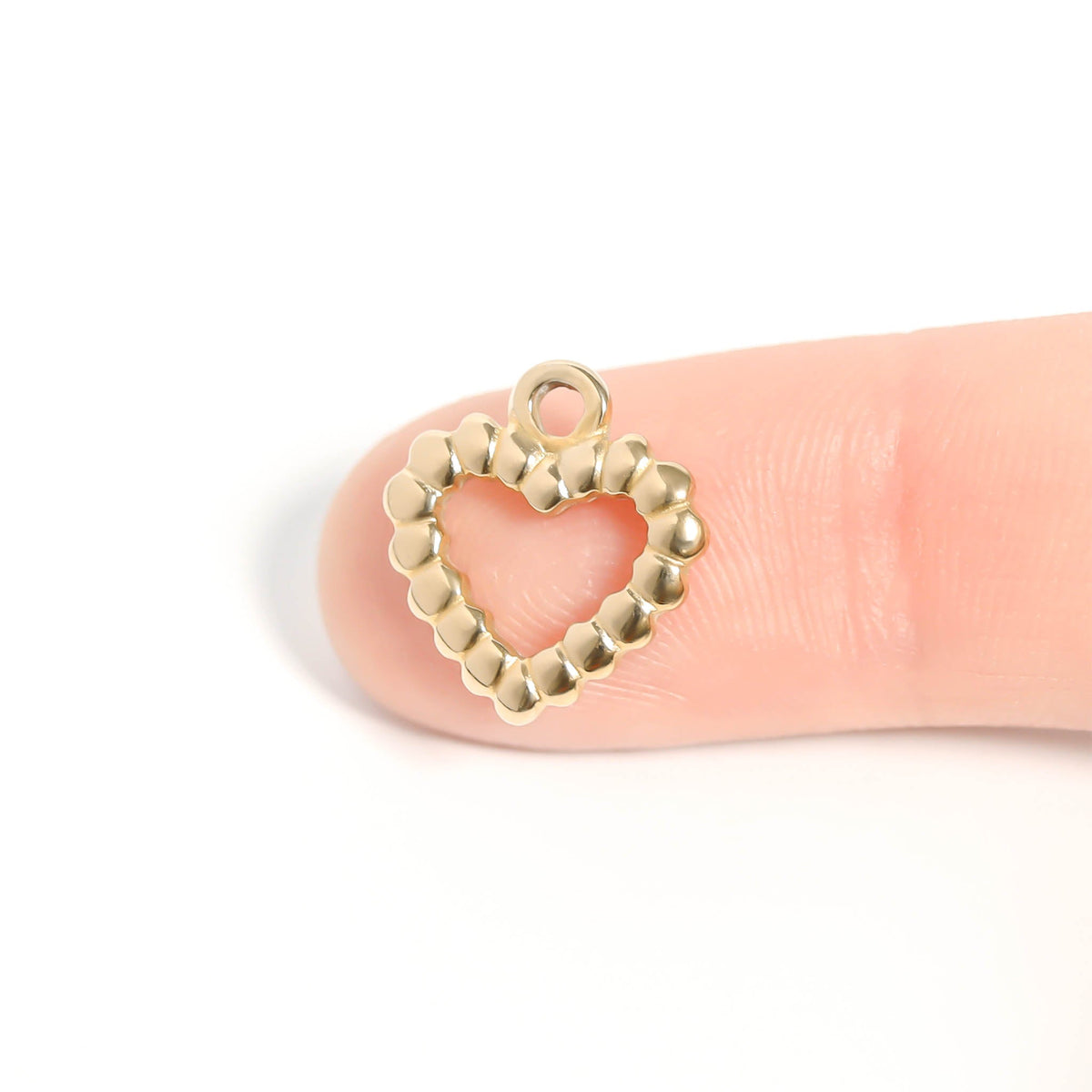 Gold heart-shaped charm on a finger against a white background