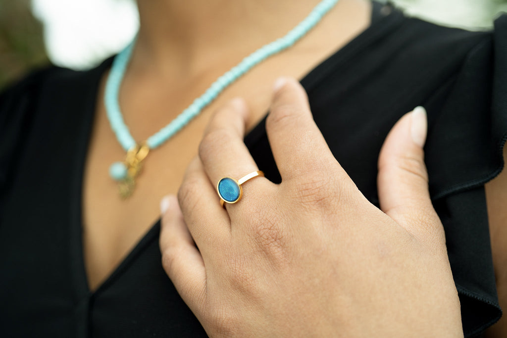 Close-up of a hand wearing a gold ring with a blue stone, with a blurred background