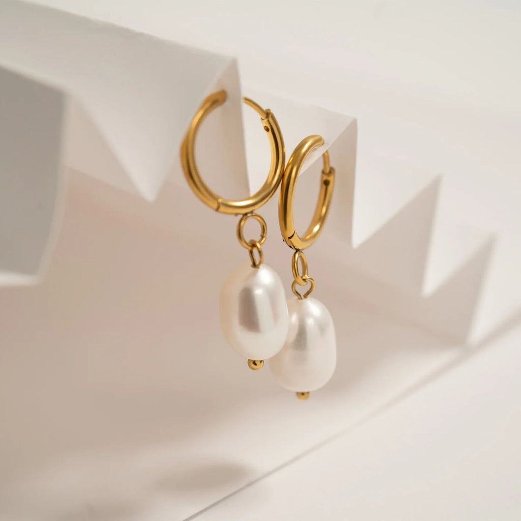 Gold hoop earrings with pearl drops on a light background
