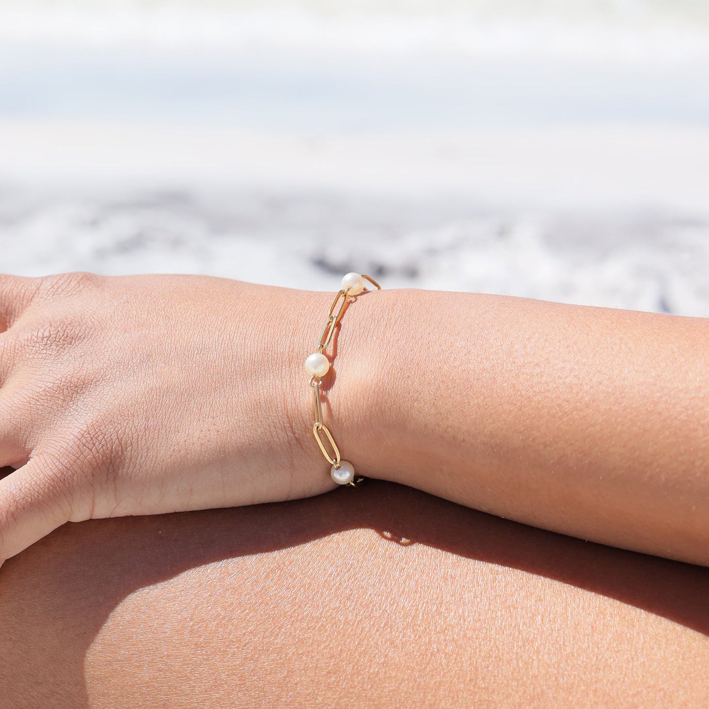 Gold bracelet with pearl beads on a wrist against a blurred natural background