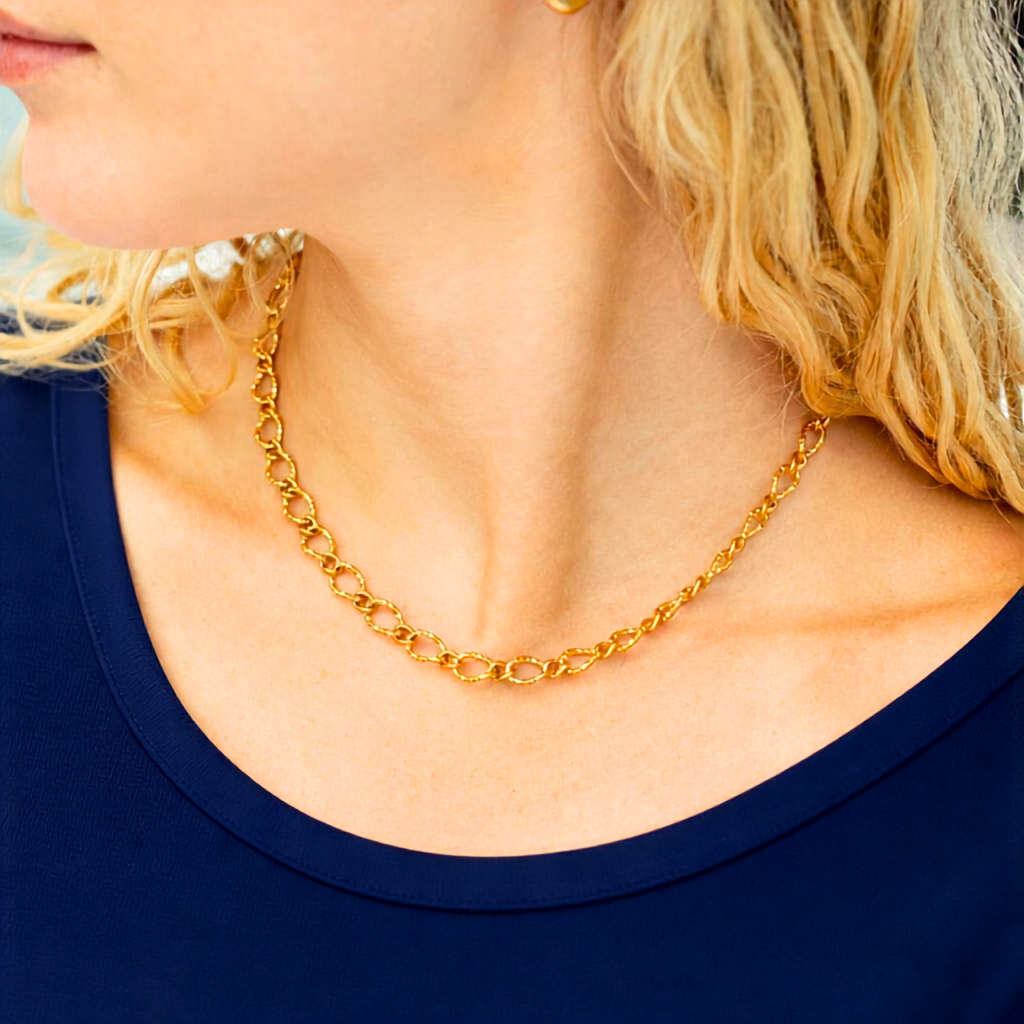A close-up lifestyle shot of a woman wearing a gold chain necklace with interlocking oval links, paired with a navy blue top.