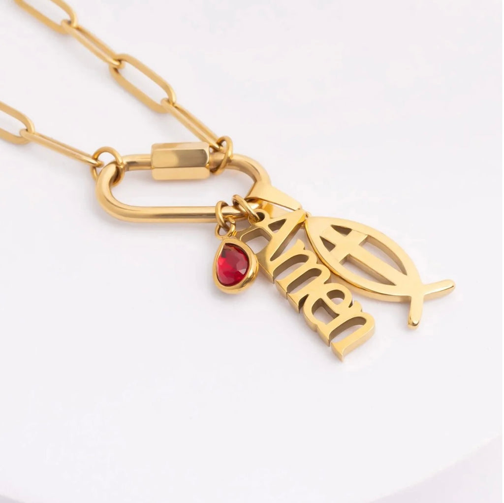 Gold-tone chain necklace with a clasp and three charms: a fish symbol, a stylized nameplate reading 'Amen', and a small red heart-shaped gemstone.