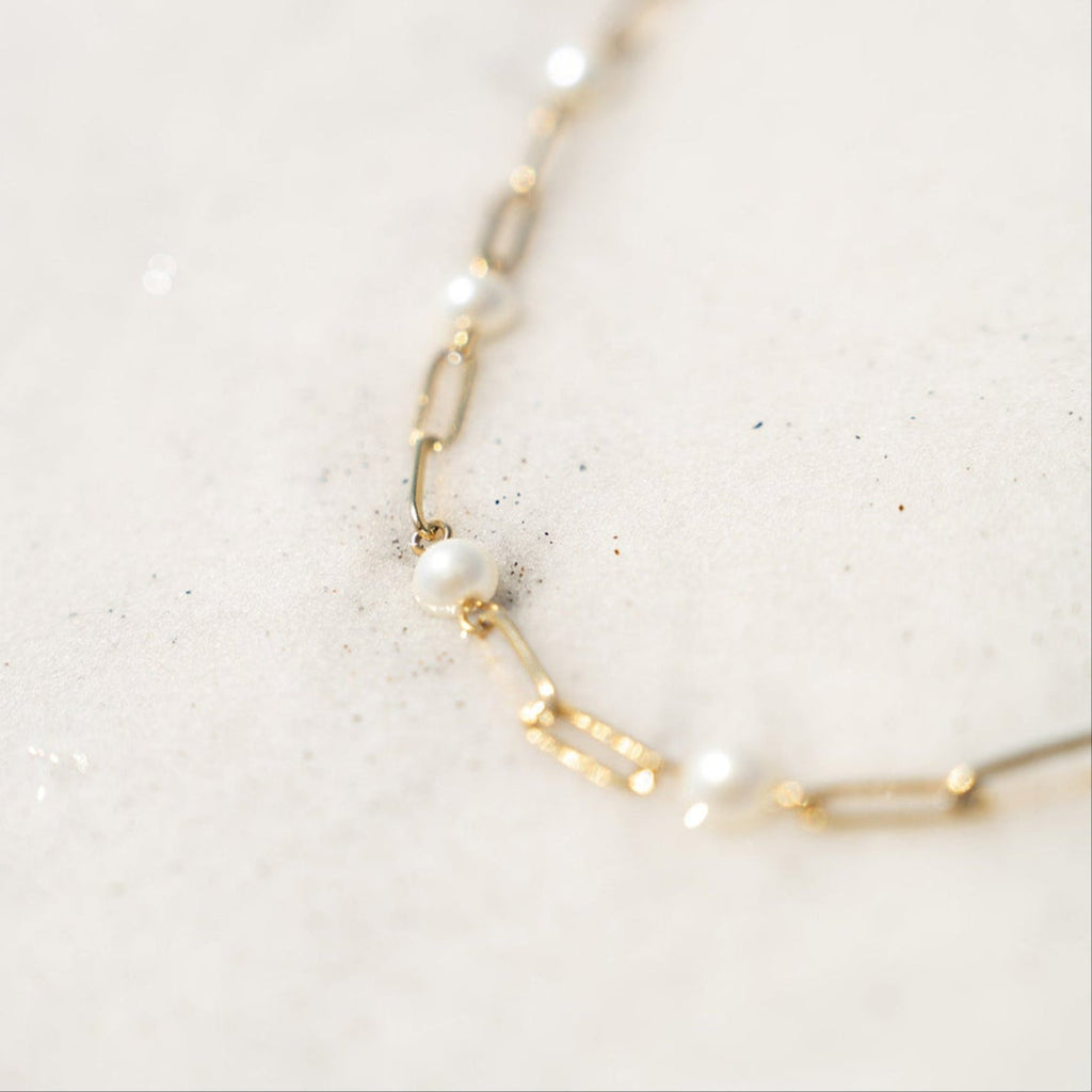 Gold chain necklace with pearls on a light marble background