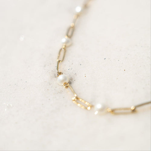 Gold chain necklace with pearls on a light marble background