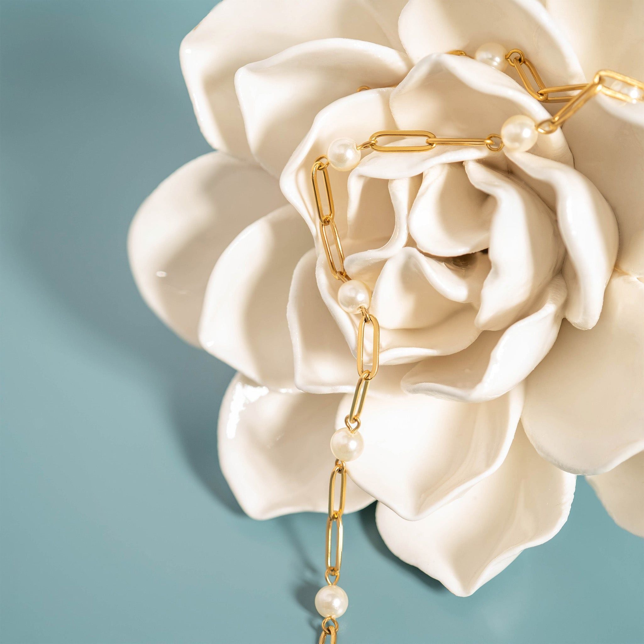 Gold chain earring with pearl drops on a white flower against a light blue background