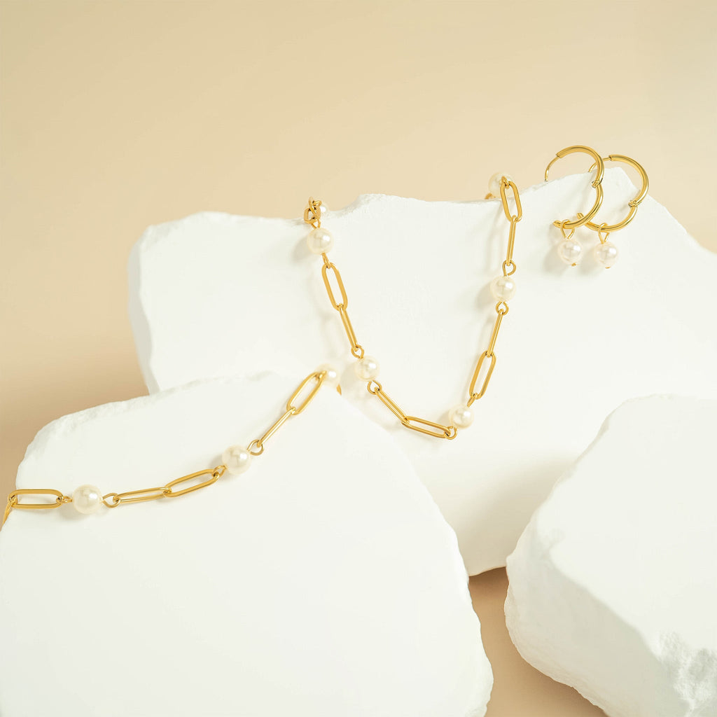 Gold necklace with pearls on a white stand against a beige background
