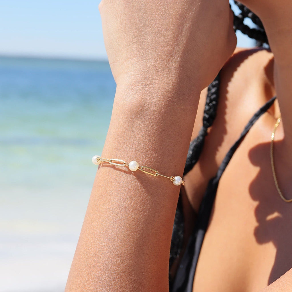 Gold bracelet with pearls on a person's wrist against a beach background