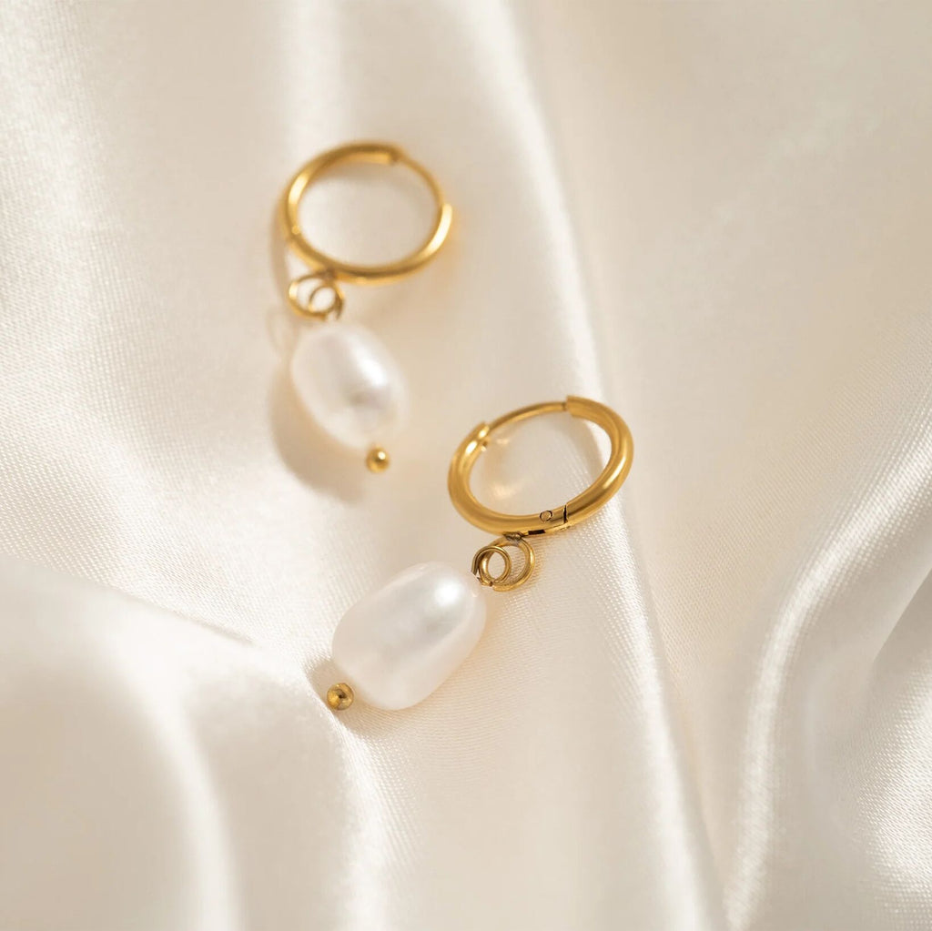 Gold hoop earrings with pearls on a satin surface