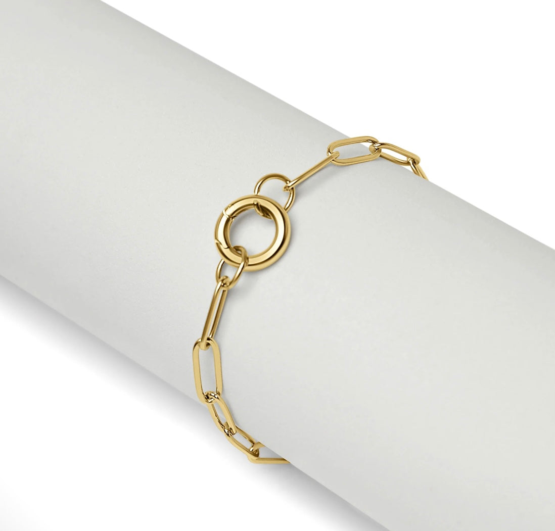 A gold paperclip chain bracelet with a double-ring clasp, displayed on a white cylindrical mannequin arm against a white background.
