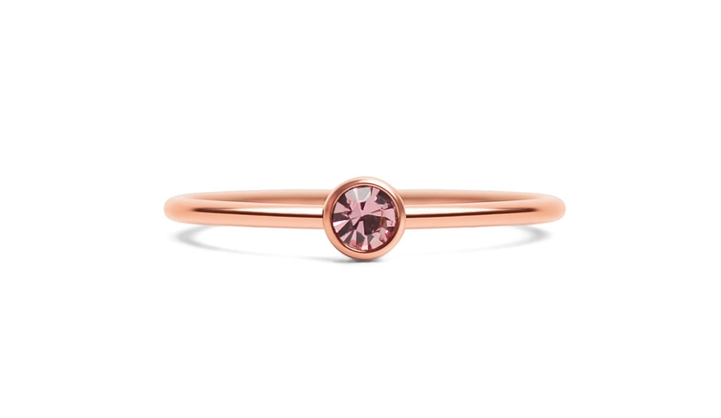 A delicate rose gold ring with a single round-cut pink gemstone in a bezel setting, shown on a clean white background.