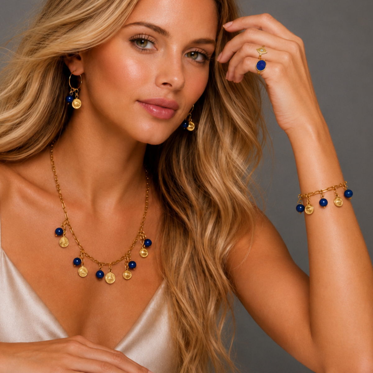 A model wearing the Mayfair Collection’s gold evil eye and blue sodalite charm earrings, layered charm necklace, matching charm bracelet, blue mood ring, and gold evil eye ring, featuring blue sodalite stones and gold evil eye charms against a neutral background.