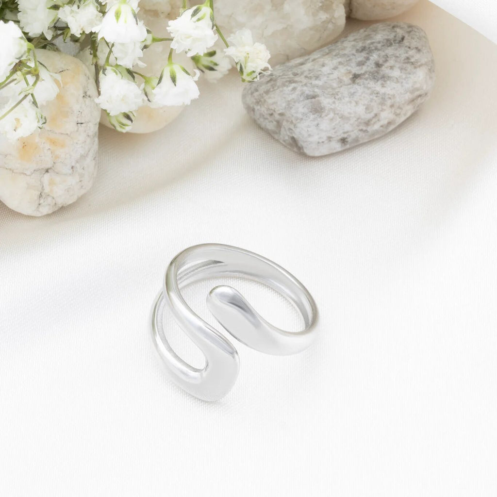 Silver ring on a white surface with stones and flowers in the background
