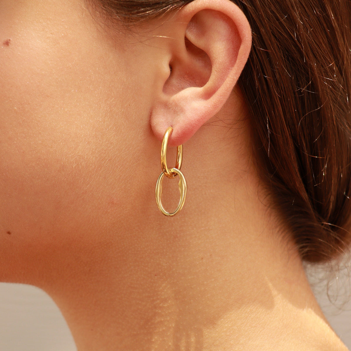Gold hoop earring worn by a person with a neutral background