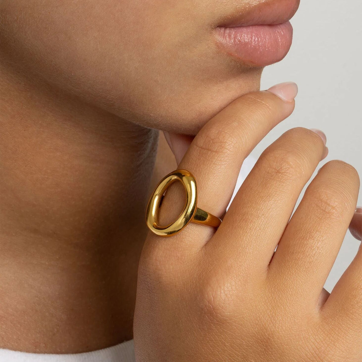 Close-up of a hand wearing a gold ring with a plain background