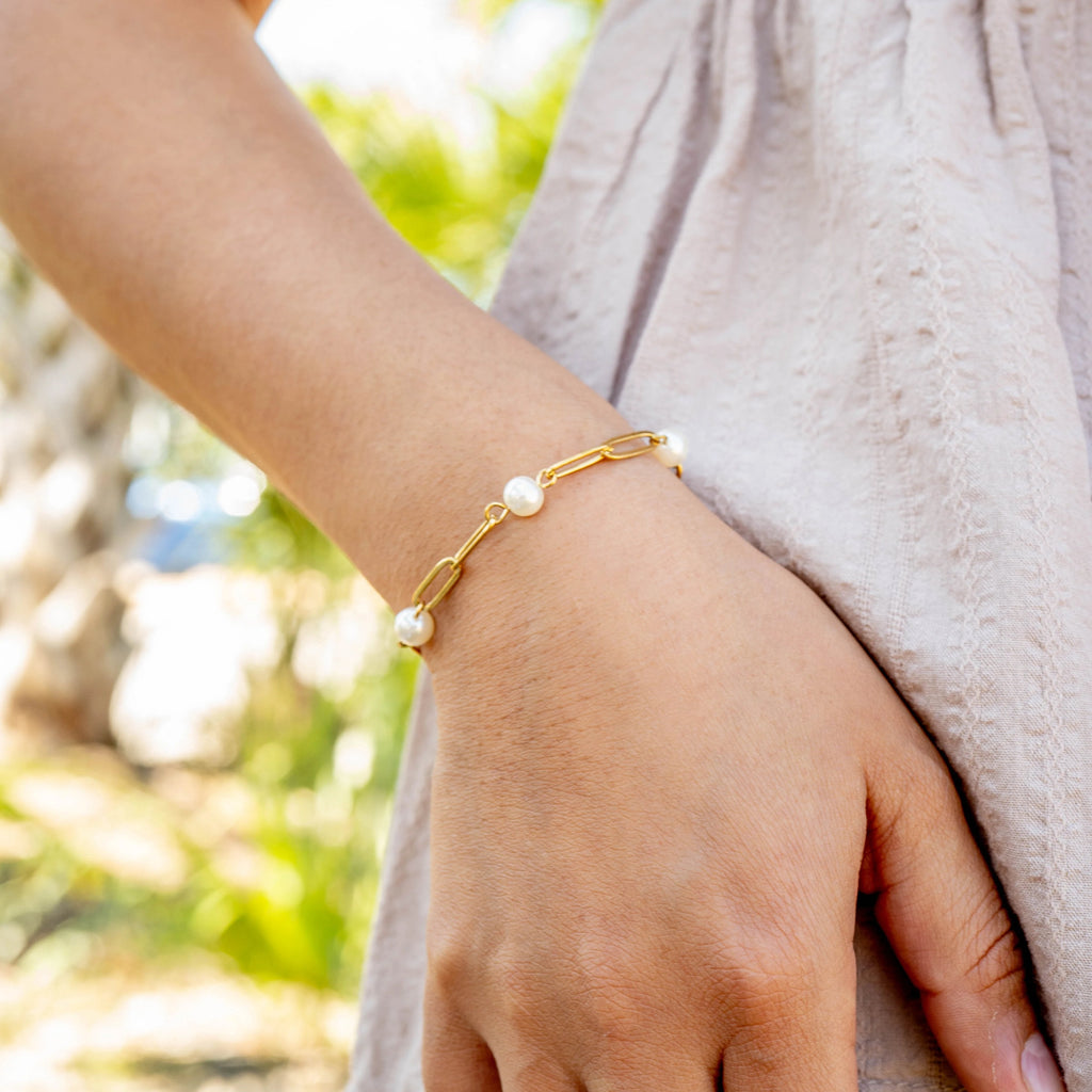 Gold bracelet with pearls on a wrist against a blurred natural background