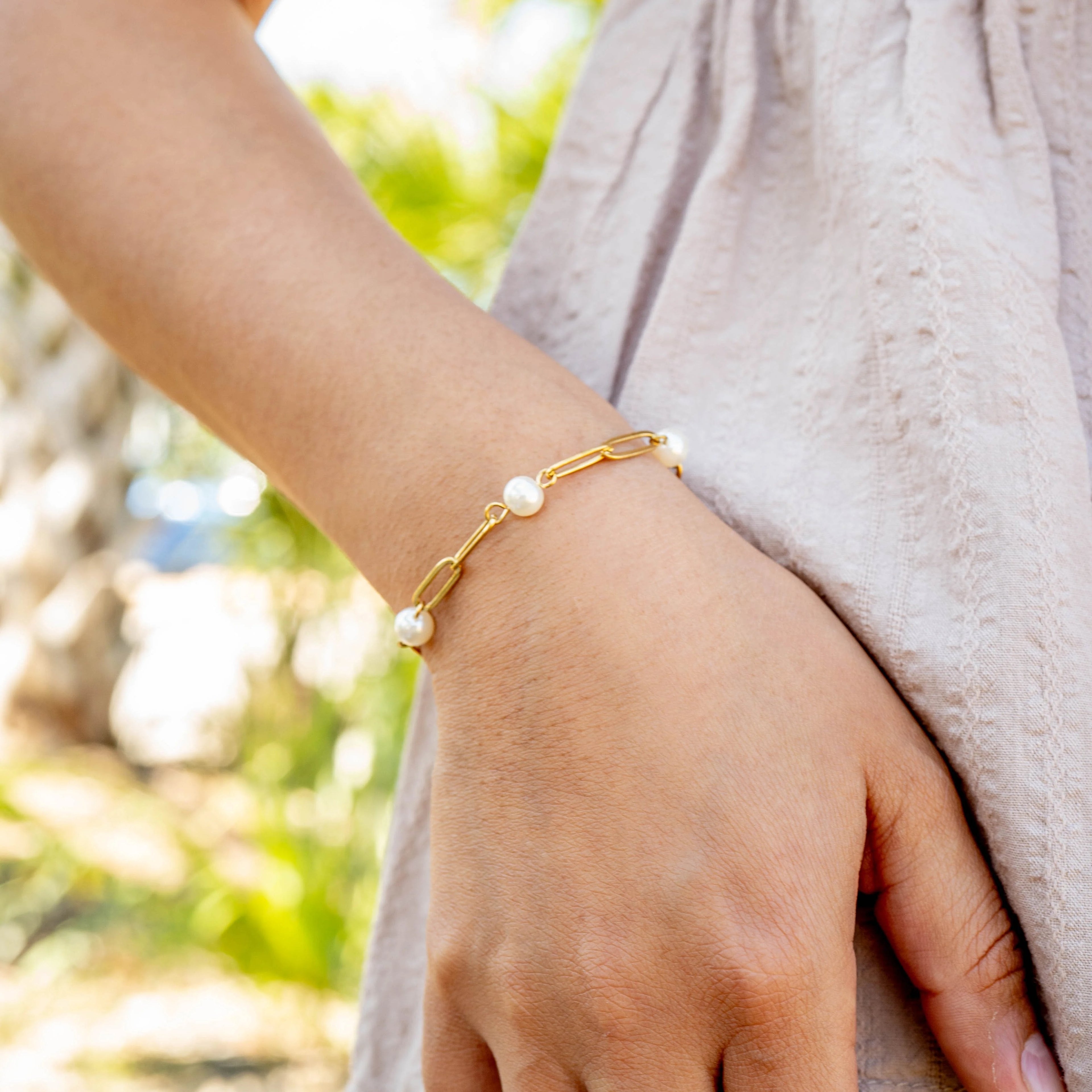 Gold bracelet with pearls on a wrist against a blurred natural background