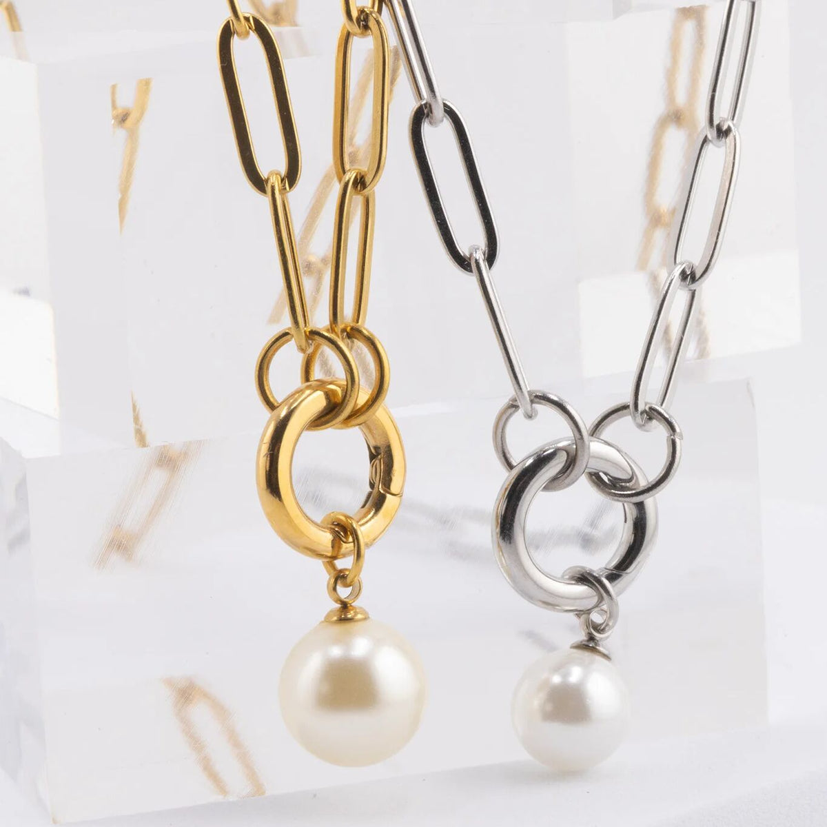 Two pearl-dangled necklaces, one gold and one silver, on a marble surface.