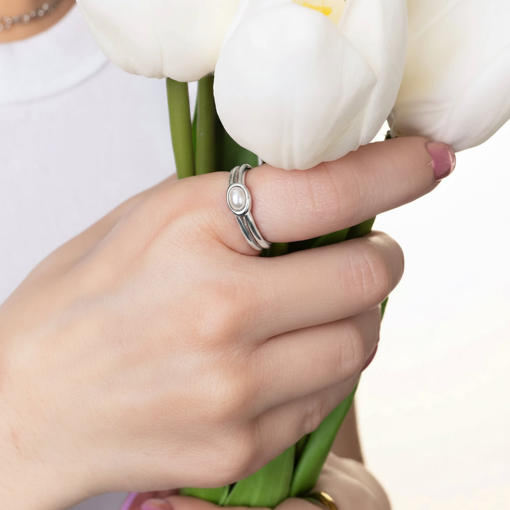 Hand holding a bouquet of white tulips with Pearl and silver ring from Garden District Jewelry on finger.