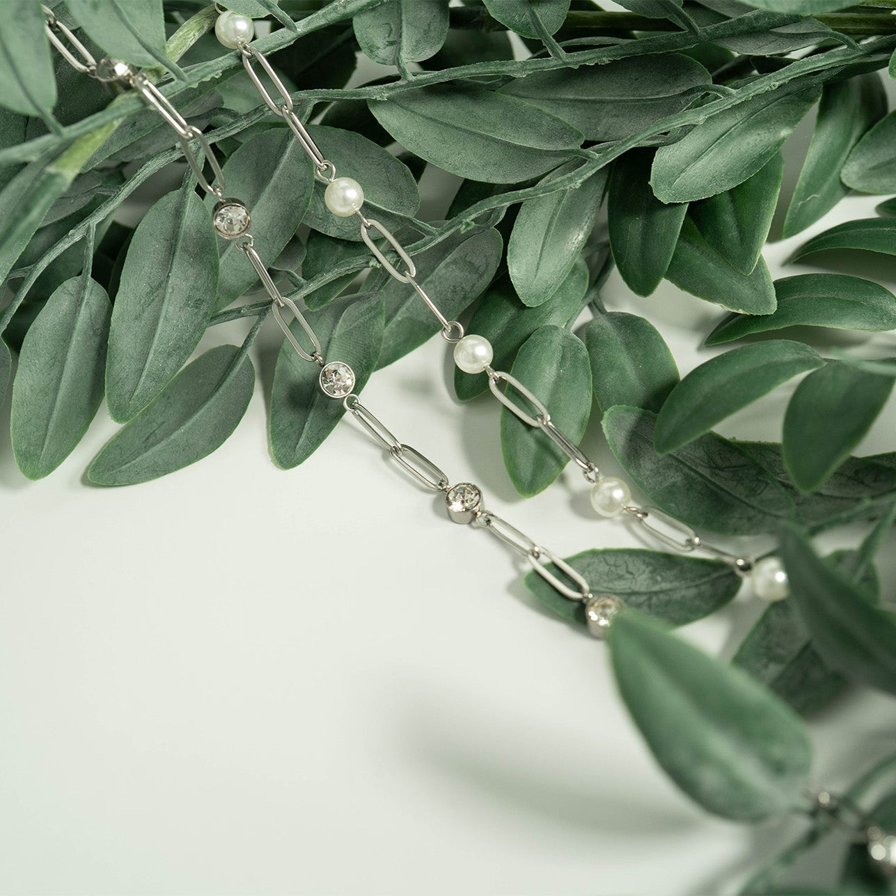 Silver chain with pearls on a green leaf background