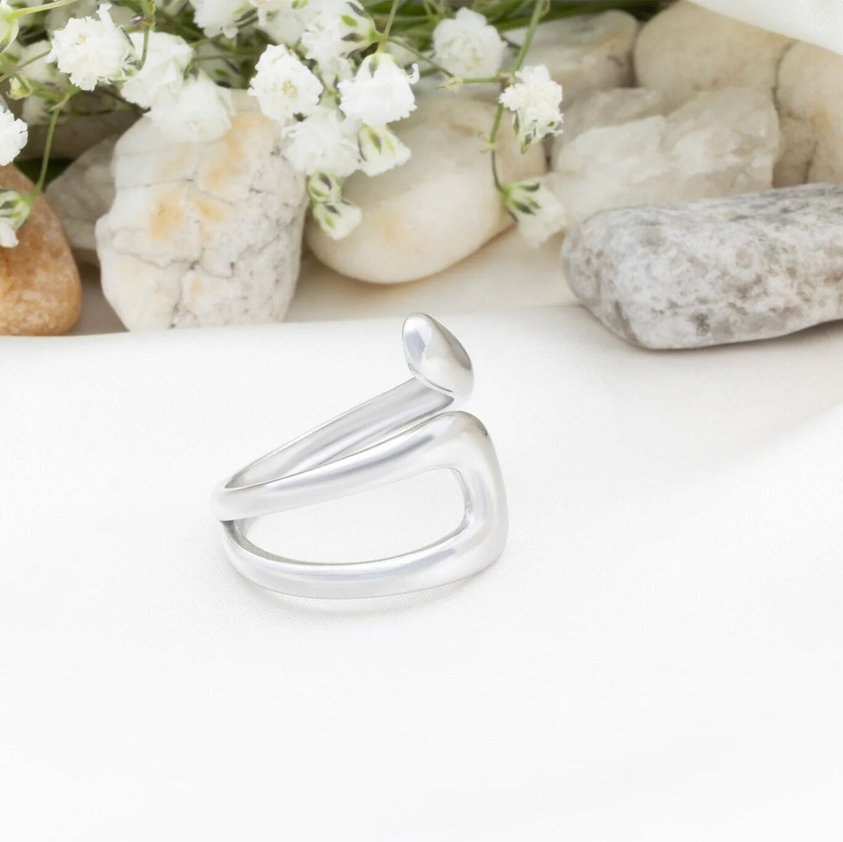 Silver ring on a white surface with stones and flowers in the background