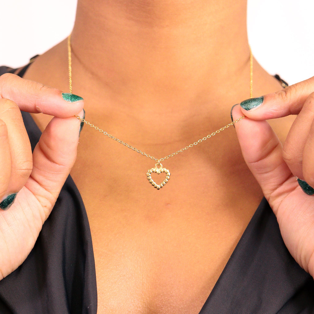 Gold heart-shaped necklace being held by a person with green nail polish.